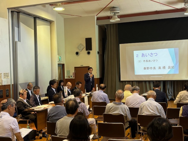 会議室で複数の参加者が椅子に座り、前方で市長がマイクを持って挨拶している様子の写真