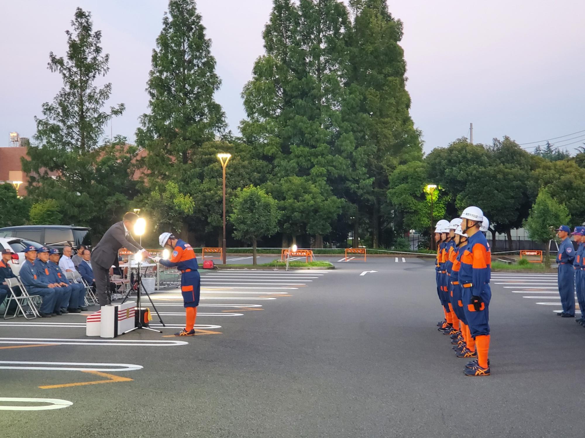 制服を着た消防団員が整列し、壇上でスーツの市長から表彰状を受け取っている写真