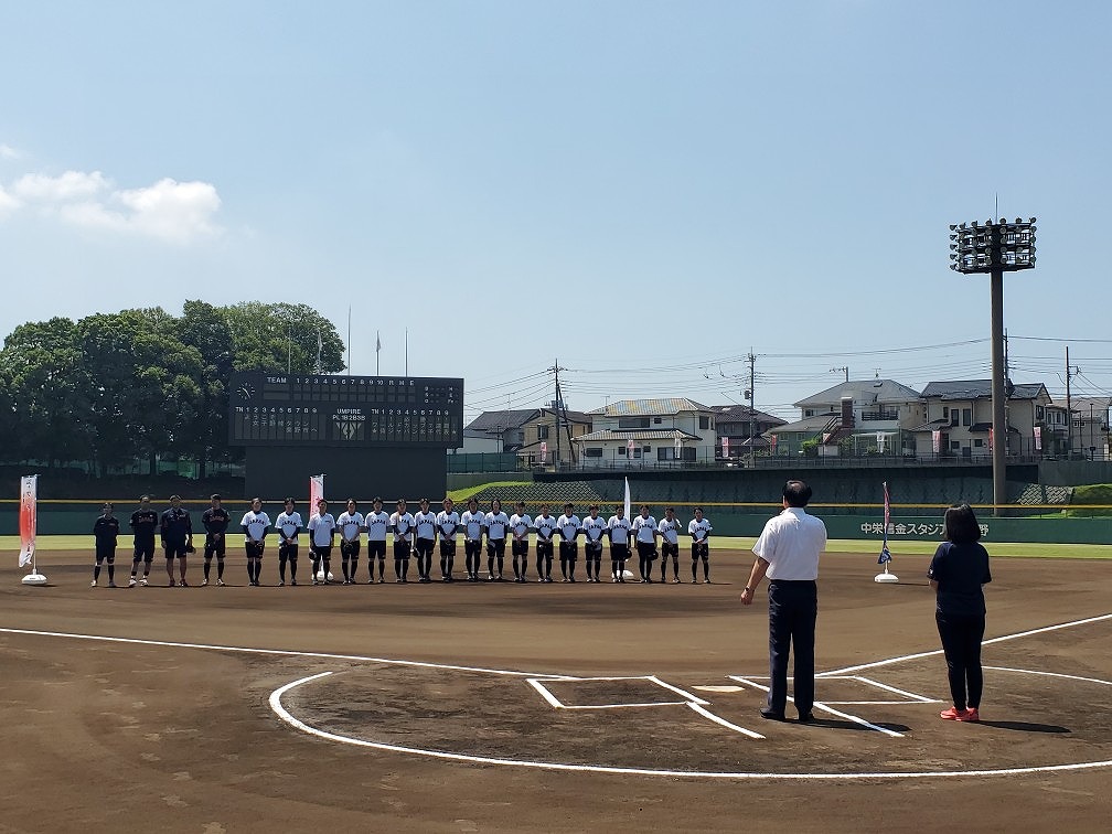 晴天の野球場で整列して一列に並び、前に2人の関係者が立っている女子野球チームの選手たちの写真