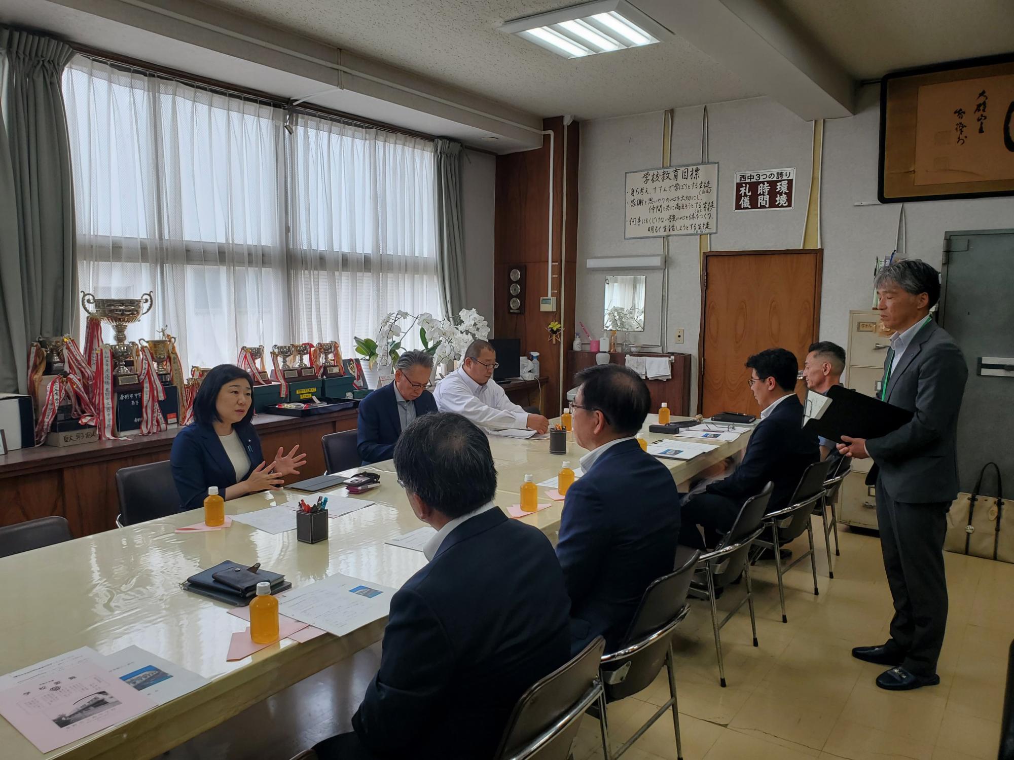 会議室で女性の来訪者が学校関係者と意見交換をしている様子の写真