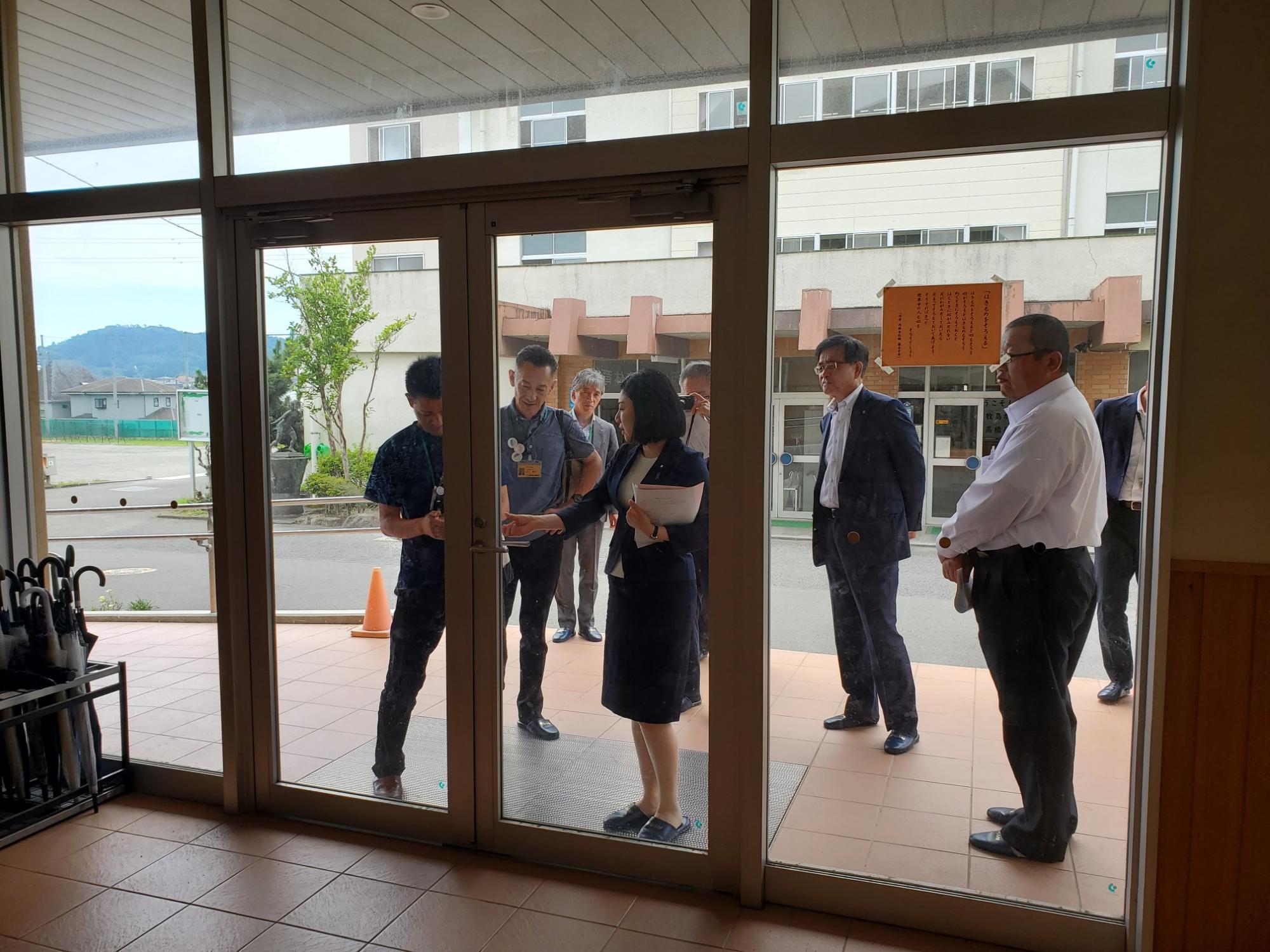 正面玄関前で来訪者一行が職員と資料を確認しながら説明を受けている様子の写真