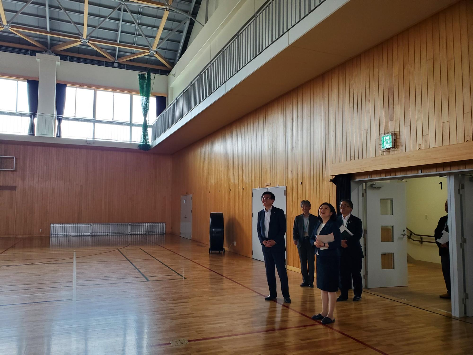 体育館内で来訪者が上部の構造などを見上げながら説明を受けている様子の写真