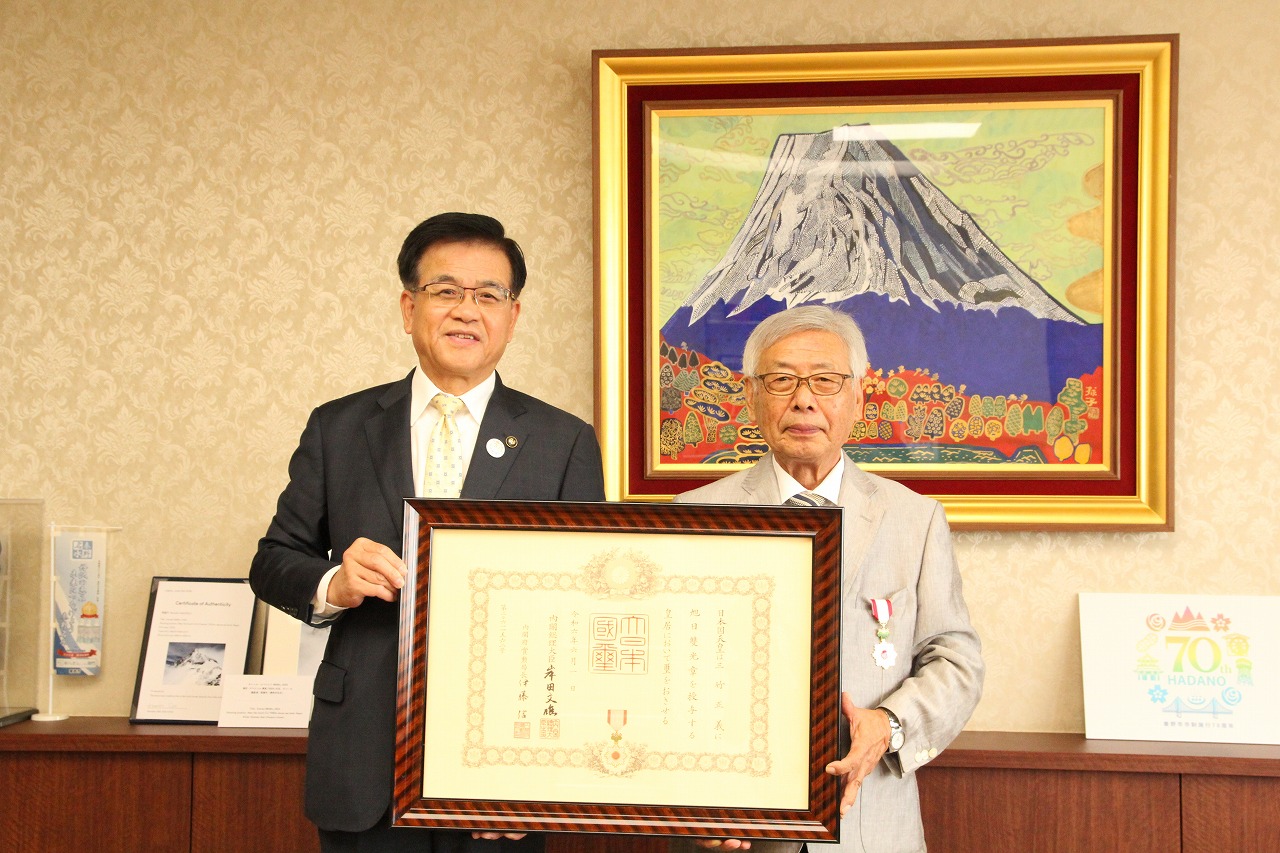 市長と三竹正義さんが並び、額に入った勲章の賞状を持って記念撮影している写真