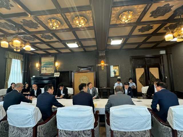 白い布がかけられた長テーブルの周囲に複数の人が座り、天井からシャンデリアが下がる豪華な洋風の部屋で、会議が行われている様子の写真