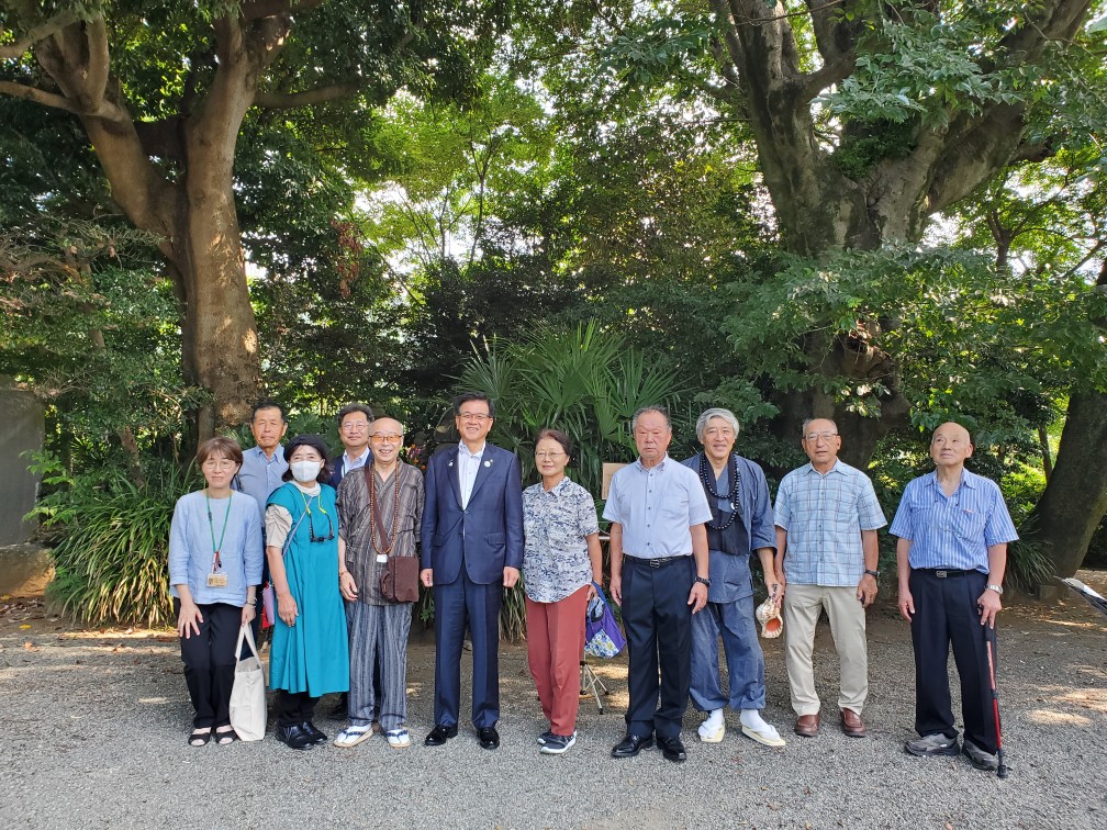 緑に囲まれた場所で、市長と地域住民達が一列に並び、笑顔で記念撮影をしている集合写真