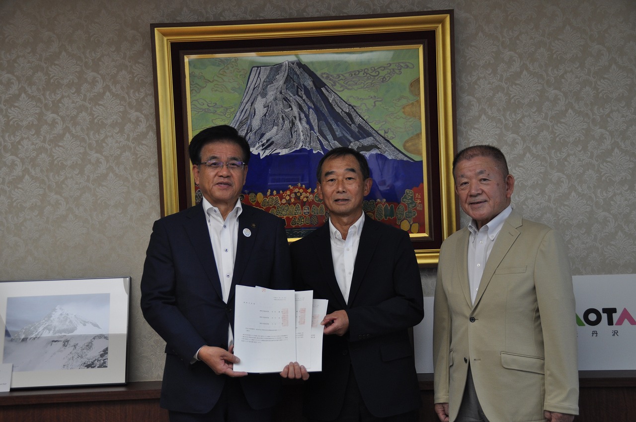 中央の市長と男性が書類を持っている、スーツ姿の男性3人での記念写真