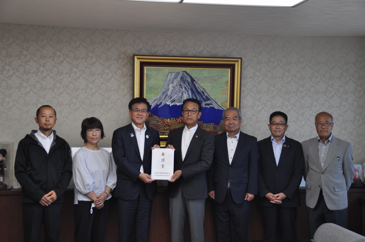 富士山の絵の前に立つ市長を含む7人の関係者が、要望書を手にして記念撮影をしている写真