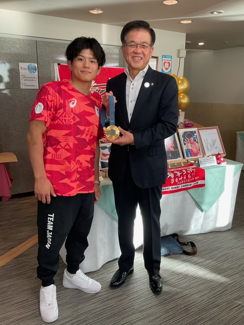 赤いTシャツを着た清岡選手と、金メダルを両手で持った市長が並んだ記念写真