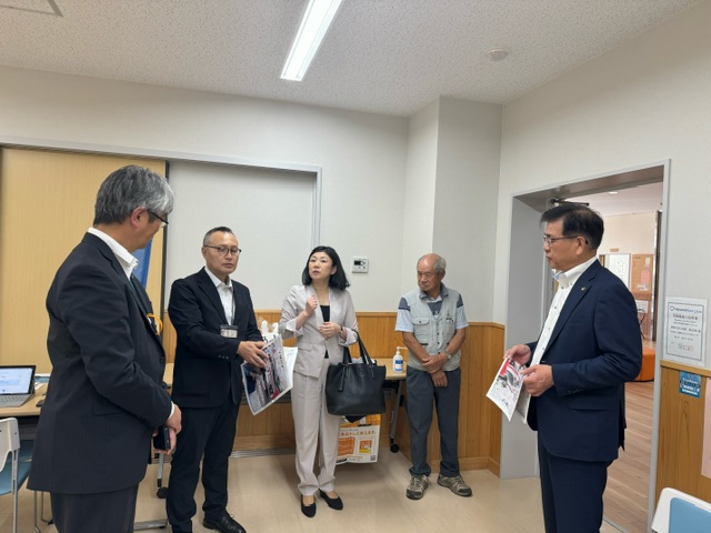 白い壁の室内で、スーツ姿の市長と男性2人、ベージュのスーツ姿の牧島かれん衆議院議員、グレーのベストを着た男性1人が立って話をしている、視察の様子の写真