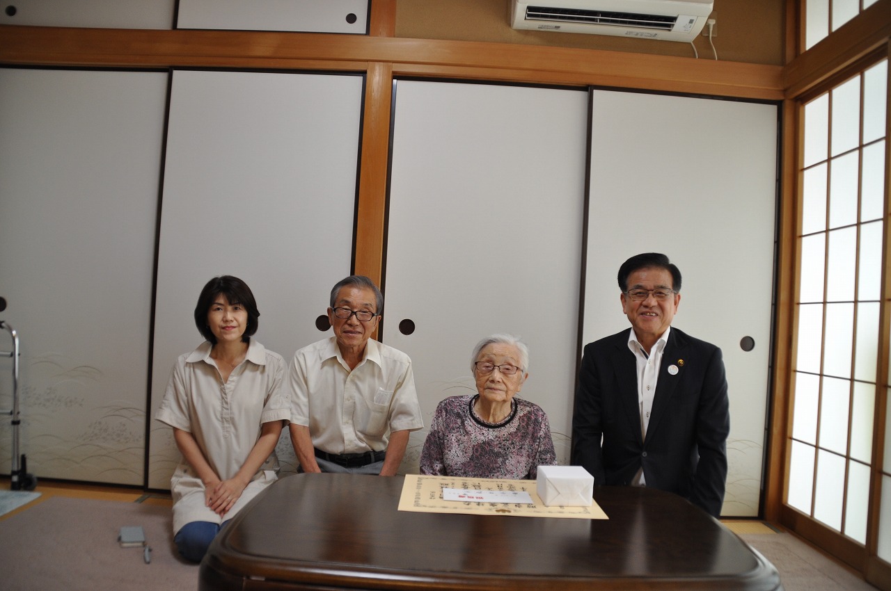 和室で座卓を前に、右から黒いスーツ姿の市長、花柄の服を着た高齢の女性、白いシャツを着た男性と女性の4人が座ってカメラに向かって微笑んでいる写真