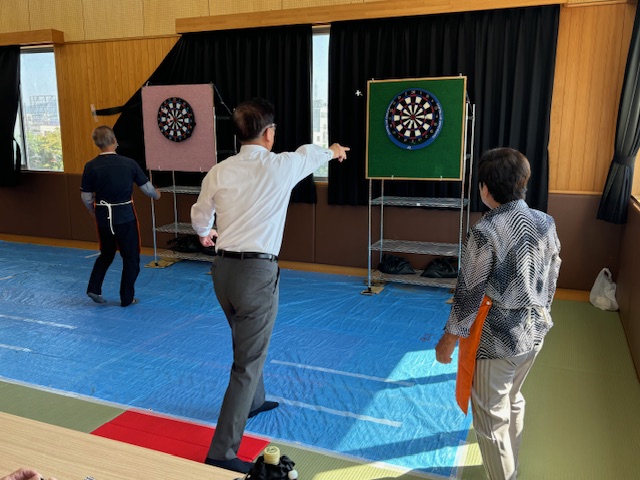 屋内の畳敷きの部屋で、二つのダーツボードに向かって複数の人がダーツを投げている様子を捉えたイベント風景の写真