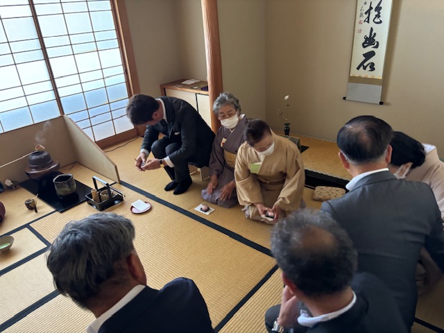 茶道具などが置かれた和室で数人の人々が正座している茶道体験の様子の写真