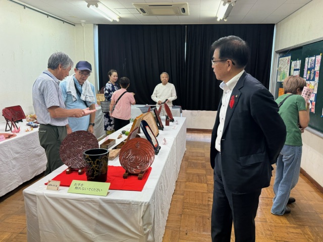 民芸品が展示された会場で、市長が他の来場者と作品を鑑賞している様子の写真