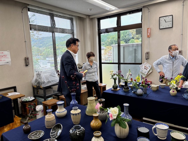 様々な陶器の壺や花瓶が並んだまつり会場で、市長が関係者と話している室内の写真