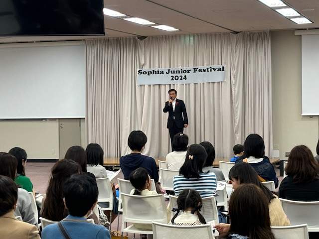 舞台上のマイク前で挨拶する市長を、多くの観客が椅子に座って見上げている「第47回ソフィア・ジュニア祭」の写真