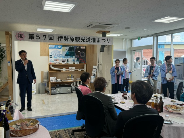 「第57回伊勢原観光道灌まつり」の懇親会で、市長がマイクを持って挨拶しており、テーブルには料理が並んでいる室内の写真