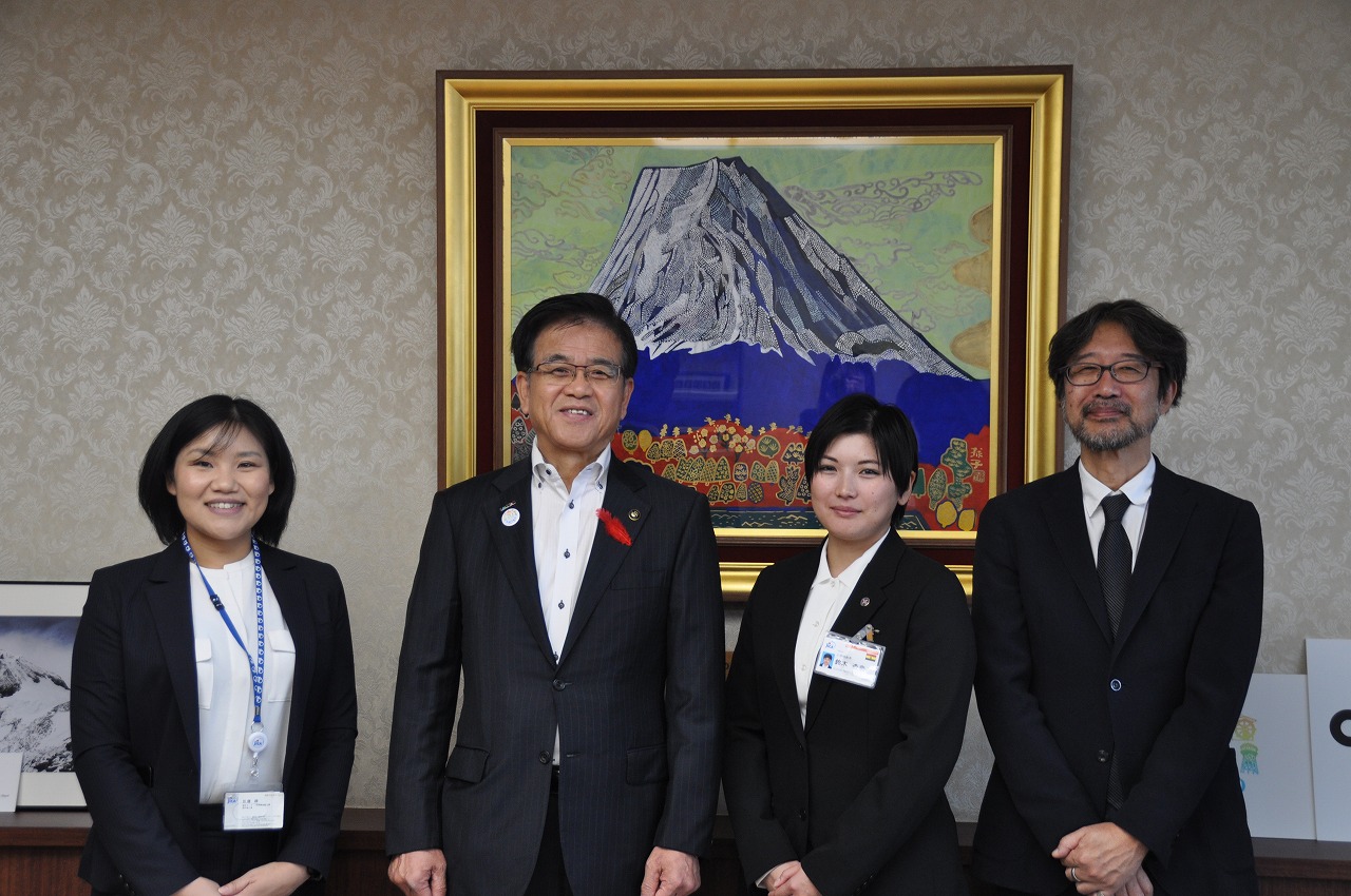 山の絵画が掛けられた壁を背に、高橋市長と岡本さんら3人の男女が並んで立っている記念写真