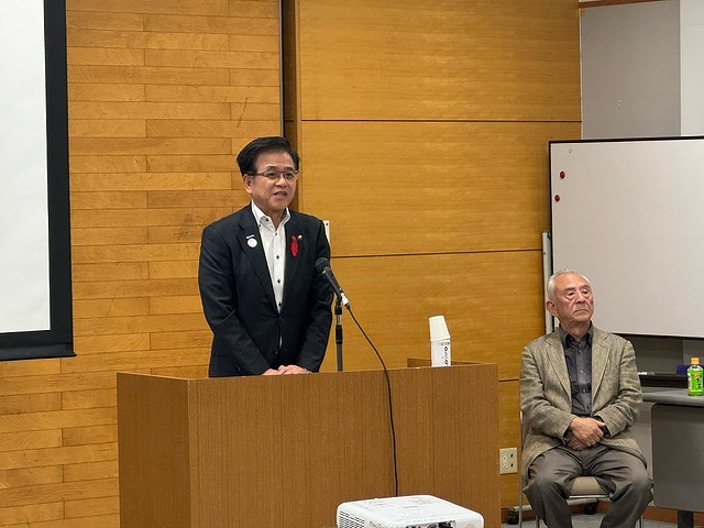 演台に立った高橋市長が話をしており、隣に小川三夫さんが座っている様子の写真