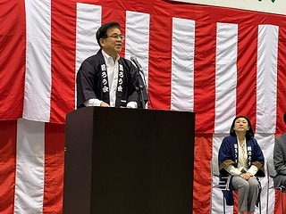 紅白幕の前の演台に立った法被姿の市長がスピーチをしている写真
