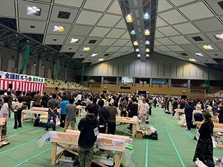 広い体育館の中に角材が置かれた台がたくさん並び、大勢の参加者で賑わっている、第40回全国削ろう会秦野大会の様子の写真