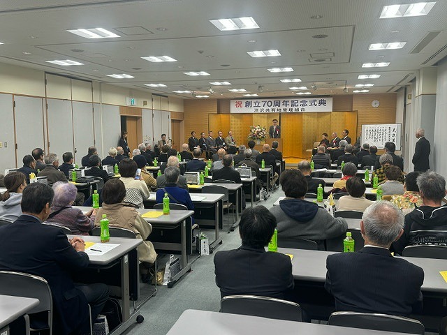 部屋の奥の「祝 創立70周年記念式典」の横断幕が掲げられた金屏風を設置した舞台に高橋市長が登壇しており、その前にたくさん並んだ長机の席には大勢の参加者たちが座っている会場全体の様子を後方から写した写真
