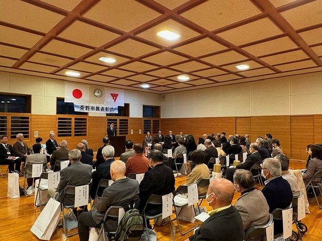 「秦野市展表彰式」と書かれた横断幕が掲げられマイクの前に立つ高橋市長の話を聞いている受賞者の方々の後方から室内全体を写した写真