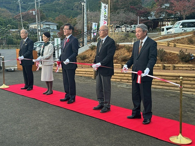 駐車場が見えるなだらかな斜面の前に敷いた赤いカーペットの上に高橋市長と4人の関係者が並び、テープカットを行っている写真