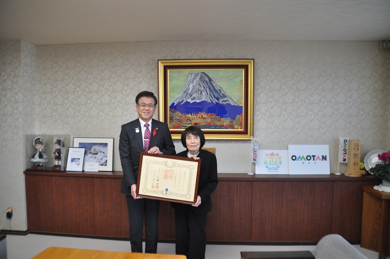 山の絵画が掛けられた壁を背に、高橋市長と府川則子さんが並んで立ち、額に入った賞状を一緒に持って写した記念写真