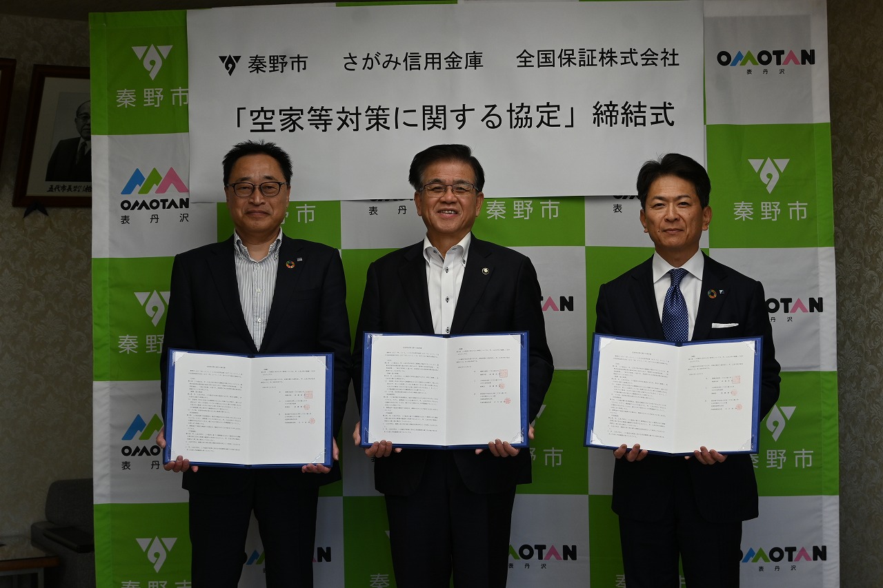 「空き家対策に関する協定」締結式で、秦野市と書かれた緑色の背景を前に、3人の男性が協定書を広げて並んでいる集合写真