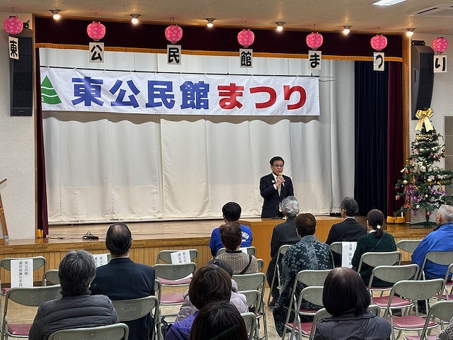 「東公民館まつり」と書かれた横断幕が掲げられた舞台の前で、市長がマイクを使って挨拶をしており、多くの来場者が着席して聞いているイベント風景の写真