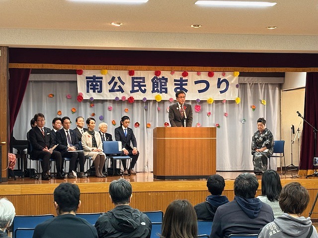 「南公民館まつり」と書かれた横断幕が掲げられた舞台上で、演台に立つ市長が挨拶をしており、他の関係者たちが着席しているイベント風景の写真