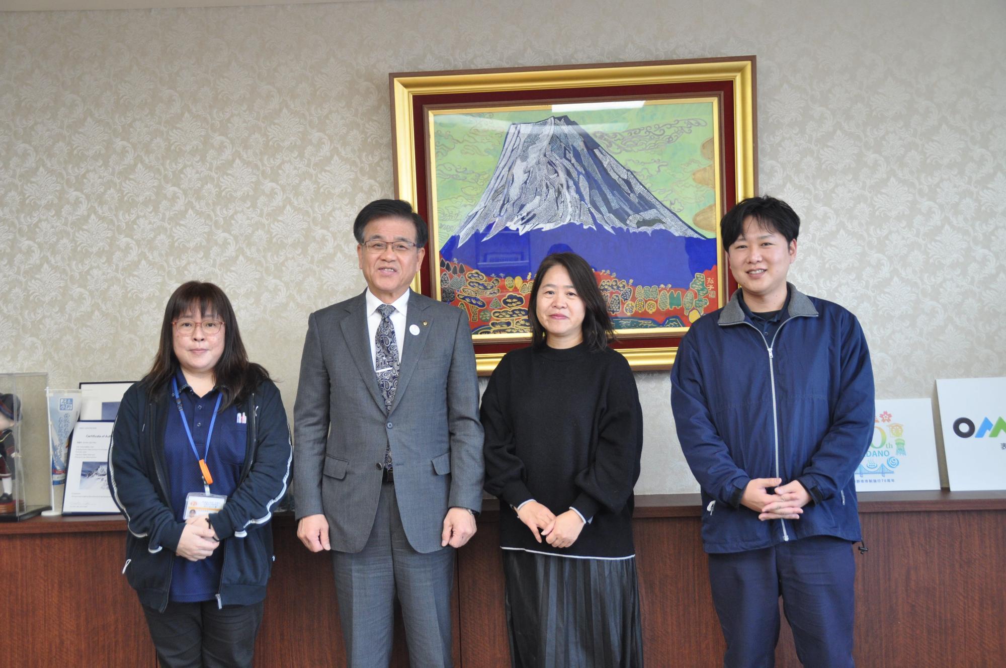 富士山の絵画が飾られた応接室で、スーツ姿の市長を中央に男女4人が並んで、全員がカメラに向かって微笑んでいる集合写真