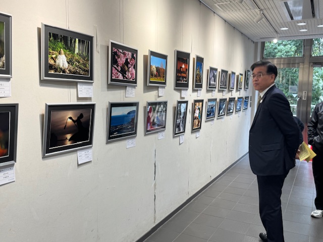 壁に飾られたたくさんの写真を見学しているスーツ姿の男性の写真