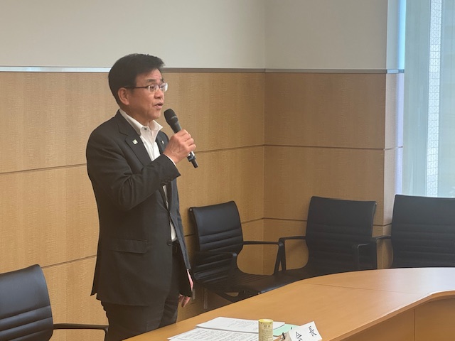 マイクを片手にスーツ姿の市長が挨拶をしている様子を斜め前方から写した写真