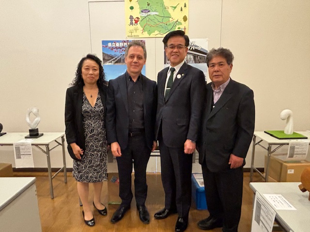 屋内にある部屋で、男女4人がカメラに向かって並んで立ち、背景には地図やポスターが掲示され、周囲には彫刻作品のような展示物やテーブルが置かれているギャラリーコンサートでの写真