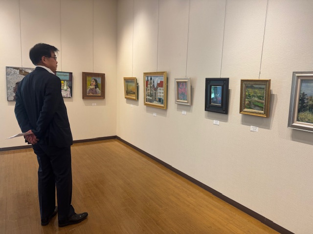 油絵や水彩画が展示されたギャラリーで、スーツ姿の市長が、壁に掛けられた作品をじっくりと鑑賞している様子の写真