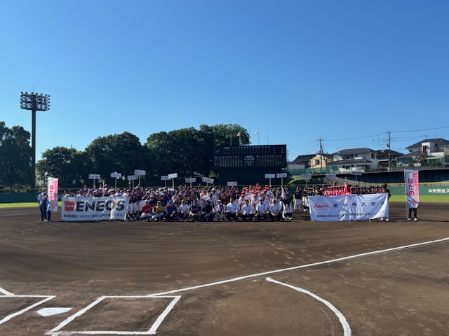 青空の広がる野球場で、ユニフォーム姿の選手たちと関係者がグラウンドに集合し、ENEOSと書かれた横断幕を持って記念撮影している写真