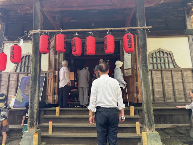 正面に「閻魔堂」の文字と赤い提灯が複数吊るされた古い寺院のような建物の入口で、白いシャツを着た市長が数人の高齢者と共に参拝のために中へ入ろうとしている様子の写真