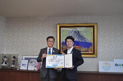 富士山の絵の前で寄付額の入った目録を持つ市長とスーツの男性。