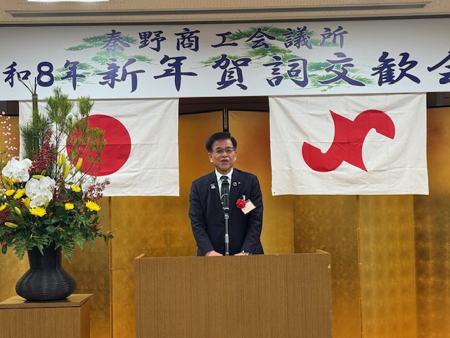 秦野商工会議所賀詞交歓会の看板の下で挨拶する市長。その左には花や松が飾られている。