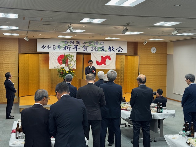 低いステージの上で挨拶する市長とそれを聞くスーツの男性多数。