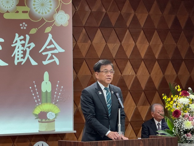 賀詞交歓会の文字が写ったスクリーンの前で挨拶をする市長。スクリーンには門松の絵も投影されている。