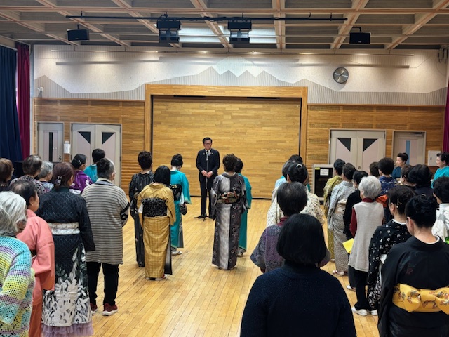 広い部屋で立って挨拶する市長と、それを聞く着物や洋服姿の女性多数