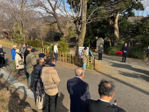 屋外で立って挨拶をする市長と、手間にコートを着た出席者10名ほどが立っている