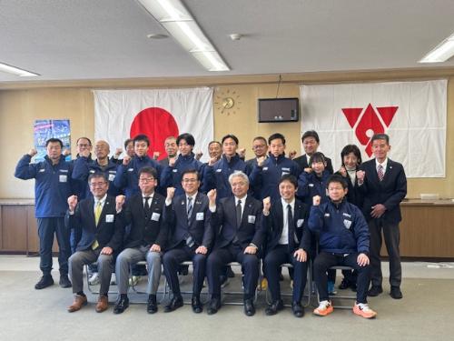 前列にスーツの男性6人、後列にジャージを着た選手とスタッフが15人立つ集合写真