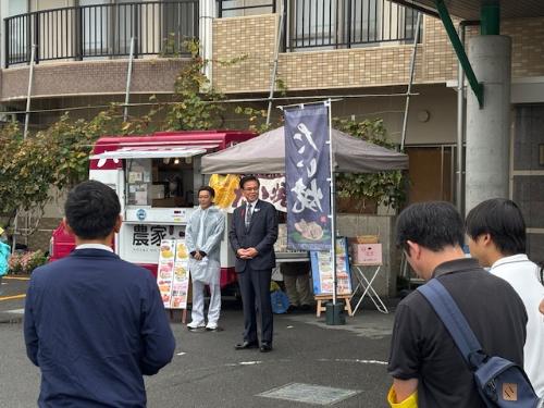 屋外のキッチンカーの前で挨拶をする市長とそれを立って聞く数名の人