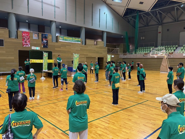 簡易ステージで挨拶する市長とそれを聞く揃いの緑色のポロシャツを着た多数の市民