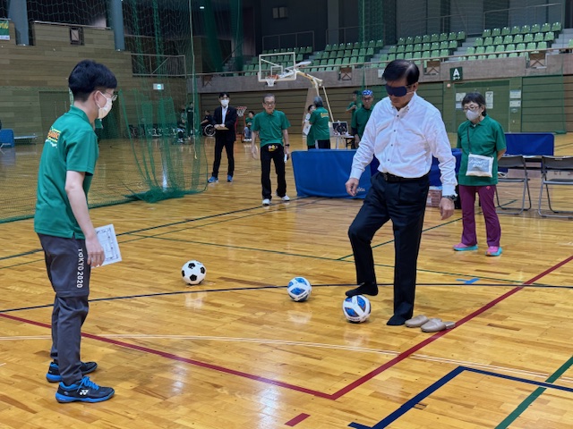 ブラインドサッカーを体験する市長とそれを教える緑のポロシャツの男性