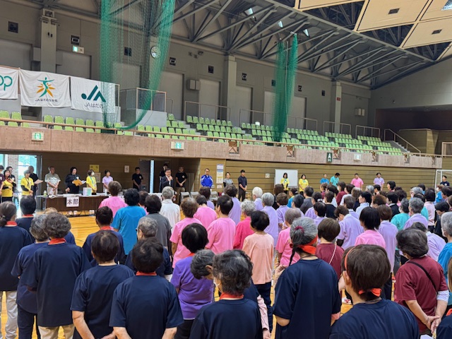 体育館に整列して市長の挨拶を聞くTシャツ姿の多数の女性たち