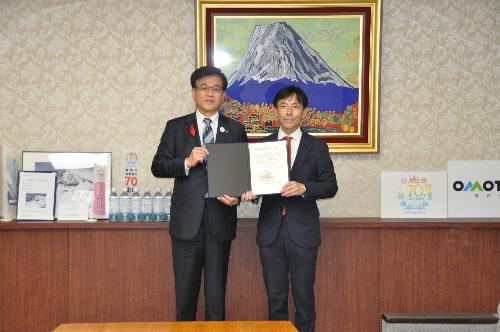 フォルダーに入れた感謝状をスーツの男性2人が持っている